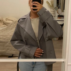 Kort trenchcoat - Jättefin helt ny oanvänd grå kort trenchcoat med lapparna kvar. Säljer för den aldrig kommit till användning tyvärr. 