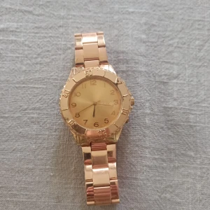 Guldfärgad klocka - Säljer en snygg guldfärgad klocka med metallarmband. Klockan har en rund urtavla med tydliga siffror och en klassisk design. Perfekt för både vardag och fest! batteriet behöver bytas.