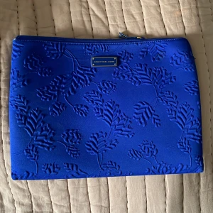 Datorfodral från Marc Jacobs  - Datorfodral från Marc Jacobs. Använt skick kan ha vissa fläckar och slitage. Dragkedjan på ena sidan är lite sönder så man får ta in när man ska öppna/stänga där men i övrigt i fint skick. Unik kornblå färg. Passar 13 tum