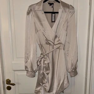 Kort satin klänning med knyte - En kort satin klänning med knyte i midjan från Boohoo som är helt oanvänd, prislappen kvar! Har ej användt den då den inte passade mig.