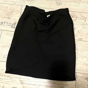 Figurnära svart kjol - Figursydd/figurnära svart kjol med design (se bild) k storlek M. Är stretchig och en minikjol.