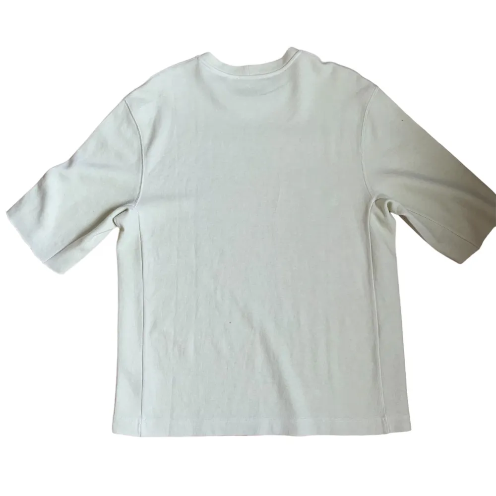 Säljer en stilren beige t-shirt från Helmut Lang med tryck på bröstet. T-shirten har en normal passform och är kortärmad, perfekt för vår och sommar. Materialet känns mjukt och skönt mot huden.. T-shirts.