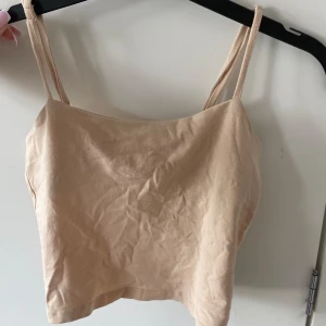 Beige linne från 157 - Säljer ett enkelt och stilrent beige linne från 157. Det är ärmlöst med smala axelband och har en tight passform. Perfekt för sommardagar eller som ett basplagg i garderoben.