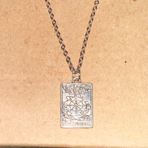 Silverfärgat halsband med rektangulär berlock - Säljer ett snyggt silverfärgat halsband med en rektangulär berlock. Berlocken har ett detaljerat mönster som ger en mystisk och unik känsla. Perfekt för att ge din outfit en extra touch!