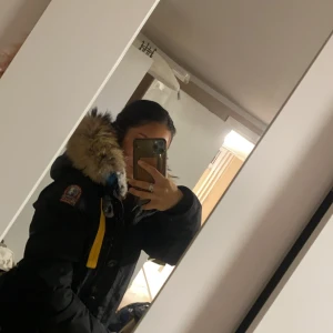 Svart vinterjacka med päls från Parajumpers - Säljer en snygg och varm svart vinterjacka från Parajumpers. Jackan har en stor huva med pälsfoder och en cool gul detalj vid halsen. Perfekt för kalla vinterdagar! 🖤Användt den bara några gånger exakt som ny, Har kartongen kvar och kvittot samt påse