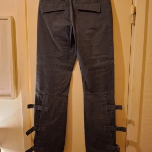 Vero Moda byxpr  - Snygga byxor med spännen på benen och fickor med dragkedja. Byxorna har en rak passform och är tillverkade i ett mjukt och bekvämt material.  Spännen från knäna och ner.