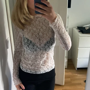 Vit spetsblus - Säljer en superfin vit spetsblus med långärmad design. Perfekt för en festlig kväll eller en stilren vardagslook. Blusen är genomskinlig och har ett vackert blommönster som ger en romantisk touch.