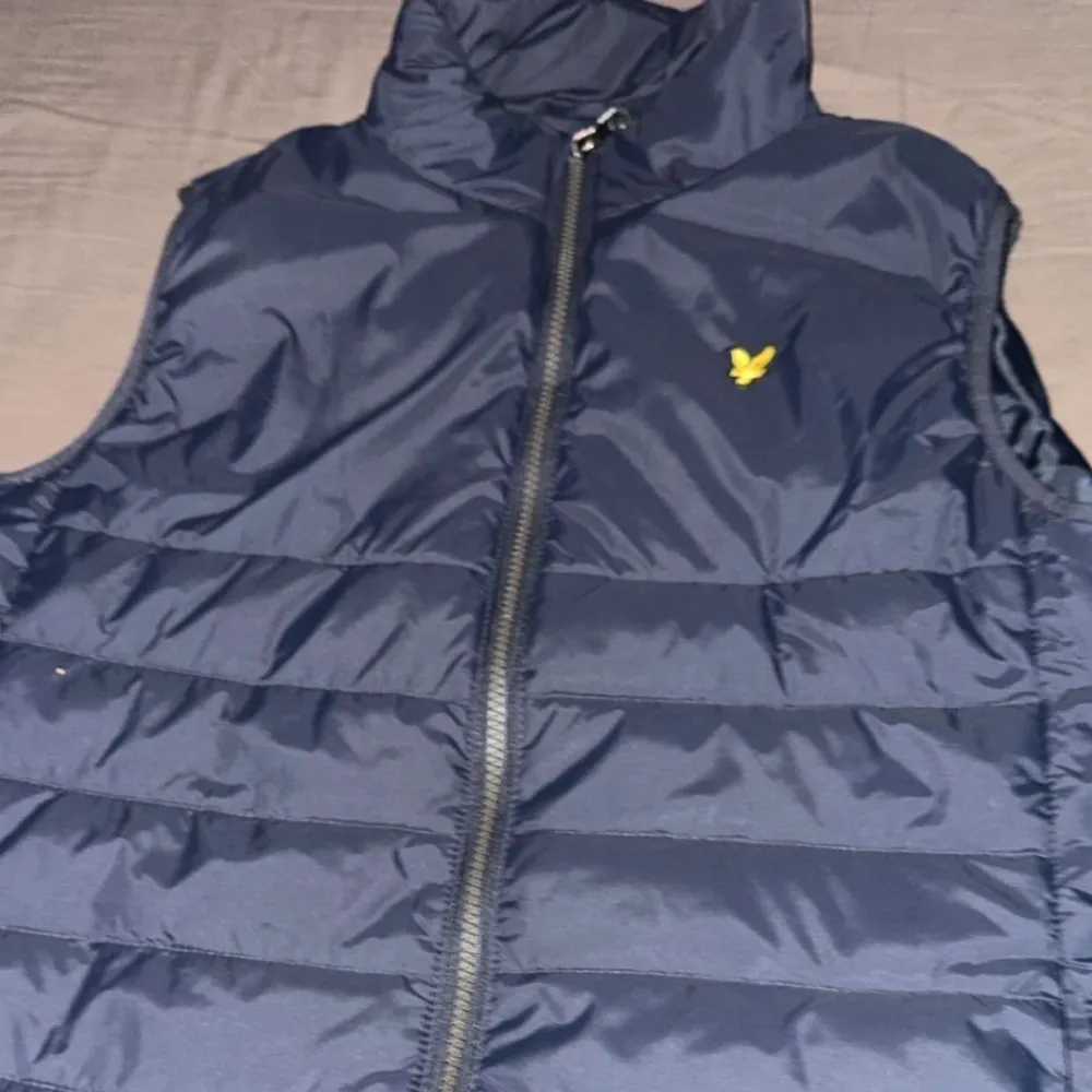 **Säljes: Mörkblå Lyle & Scott väst**  Stilren och tidlös väst från Lyle & Scott i en elegant mörkblå färg. Perfekt för lager-på-lager under kyliga dagar eller som ett lätt ytterplagg på våren och hösten. Storleken på västen är för 13-14 åringar.. Jackor.