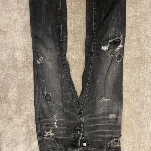 Svarta jeans från Dsquared2 - Säljer ett par svarta jeans från Dsquared2 med en cool distressed look. De har flera slitningar och hål för en edgy stil. köpta på NK för 7500kr inget kvitto tyvärr. Perfekta för en avslappnad och trendig outfit! Äkta såklart!