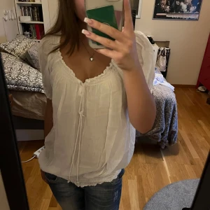 Vit blus med spetsdetaljer - Säljer en söt vit blus med jättefina detaljer och knytning framtill. tröjan sitter lite stort men ändå snyggt på mig som har storlek s. Blusen har korta ärmar och en luftig passform. Blusen är i bomull och känns väldigt bekväm att ha på sig!