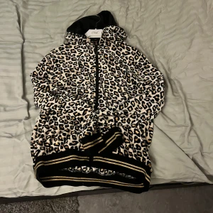 Leopardmönstrad jacka med huva - Säljer en supercool leopardmönstrad jacka med huva. Den har dragkedja framtill och ribbade muddar i svart och guld. Perfekt för att sticka ut i mängden och hålla sig varm samtidigt. Passar perfekt för höst och vår!