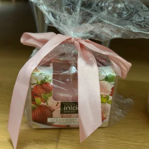 Doftljus Strawberry Dream från Inicio - Säljer ett supergulligt doftljus från Inicio med doften Strawberry Dream. Ljuset är rosa och kommer i en söt förpackning med jordgubbsdesign. Det är inslaget i cellofan med en ljusrosa rosett. Perfekt för att skapa en mysig stämning hemma! 🍓✨
