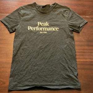 Säljer en svart t-shirt från Peak Performance i storlek M (ganska liten i storleken så passar även S). Den har en klassisk rund hals och korta ärmar. På framsidan finns texten 'Peak Performance Est. 1986' i vitt. T-shirten är i bra skick och redo för en ny ägare! Inga fläckar eller hål.