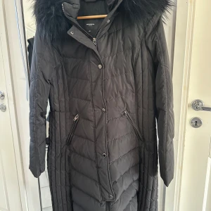 Svart lång dunjacka från Rockandblue - Säljer en svart lång dunjacka från Rockandblue i mycket bra skick. Jackan har en mysig pälskantad huva och stängs med både dragkedja och knappar vilket gör den avtagbar. Fickorna är även fodrade.Perfekt för kalla vinterdagar! 🖤