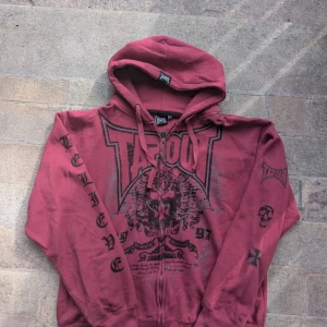 Röd Tapout Hoodie - Säljer en cool röd hoodie från Tapout med tryck på framsidan och ärmarna. Den har en stor luva och är perfekt för en avslappnad stil. Passar bra till både träning och vardag. Skön och bekväm att ha på sig. Tryck på armen, "believe" och andra symboler på andra. Storlek XXL Skick: Den är i nyskick men har använts. Hör av dig om du är intresserad! 🔥