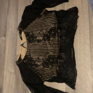 Svart spetsblus från Bik Bok - Snygg svart spetsblus från Bik Bok med blommigt mönster och transparenta detaljer. Perfekt för en festlig kväll! Blusen har långa ärmar och en elegant design som ger en chic look.