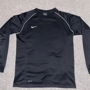 Säljer en svart långärmad tröja från Nike med Dri-FIT teknologi. Perfekt för träning eller vardagsbruk. Den har en enkel design med en vit Nike-logga på bröstet och kontrastsömmar. Superbekväm och andas bra!