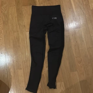 Svarta träningstights från ICANIWILL - Säljer ett par svarta träningstights från ICANIWILL i storlek S. De är tillverkade i en mix av polyamid och polyester med elastan för extra stretch. Tightsen har en hög midja och meshdetaljer på sidorna för bättre ventilation. Perfekta för gymmet eller löprundan!