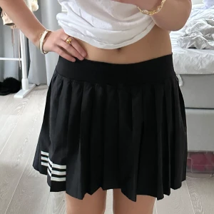 Svart tenniskortkjol adidas - Säljer en superfin svart kortkjol Adidas med tre vita ränder på sidan. Kjolen har en plisserad design som ger en snygg och sportig look. Tror storleken är S eller M. Nypris är 549kr. Bra skick!