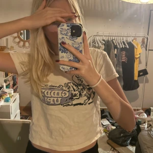 Vit babytee med cowboytryck - Säljer en cool vit t-shirt med ett unikt cowboytryck och texten 'Giddy Up!'. Den är kortärmad och har en avslappnad passform, perfekt för en casual look. Materialet känns mjukt och bekvämt, idealiskt för sommardagar. Passar bra till jeans eller shorts för en avslappnad stil.