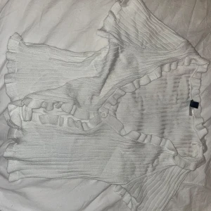 Vit ribbad kofta från Divided - Säljer en superfin vit ribbad kofta från Divided. Den har volangdetaljer längs kanterna och knappar framtill. Perfekt för vår och sommar, och den är i mycket bra skick. Passar både till vardags och fest! 🌸