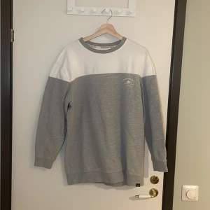 Grå och vit tröja från Newport Bay - Säljer en snygg grå och vit tröja från Newport Bay Sailing Club. Den har ett tryck på bröstet med texten 'Newport Bay Sailing Club 1985'. Tröjan är i mycket bra skick och perfekt för en avslappnad stil. Pris går alltid att förhandlas!