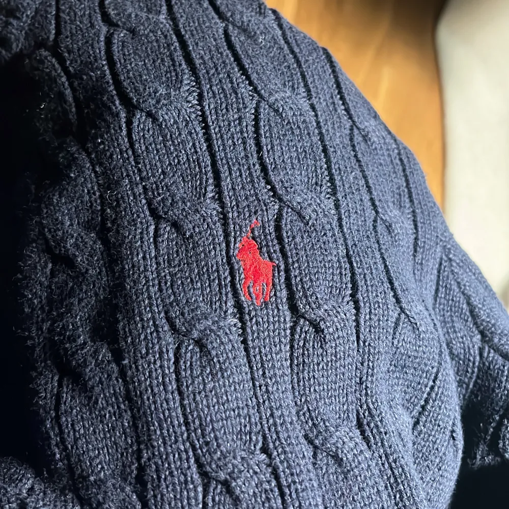 Säljer en snygg mörkblå stickad tröja från Ralph Lauren. Den har ett klassiskt kabelstickat mönster och en liten röd broderad logga på bröstet. Perfekt för höst och vinter, med långa ärmar och ribbade kanter. Passar både till vardags och lite finare tillfällen. 🧶. Tröjor & Koftor.