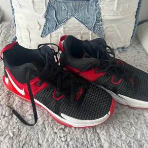 Nike sneakers i svart och rött - Säljer ett par snygga Nike sneakers i svart och rött. Skorna har en cool design med rutigt mönster och tydliga röda detaljer. De är i bra skick och perfekta för träning eller vardagsbruk. Sulan har ett häftigt mönster för bra grepp. Passar dig som vill ha stil och komfort i ett! Hör gärna av er om ni har frågor. 😊