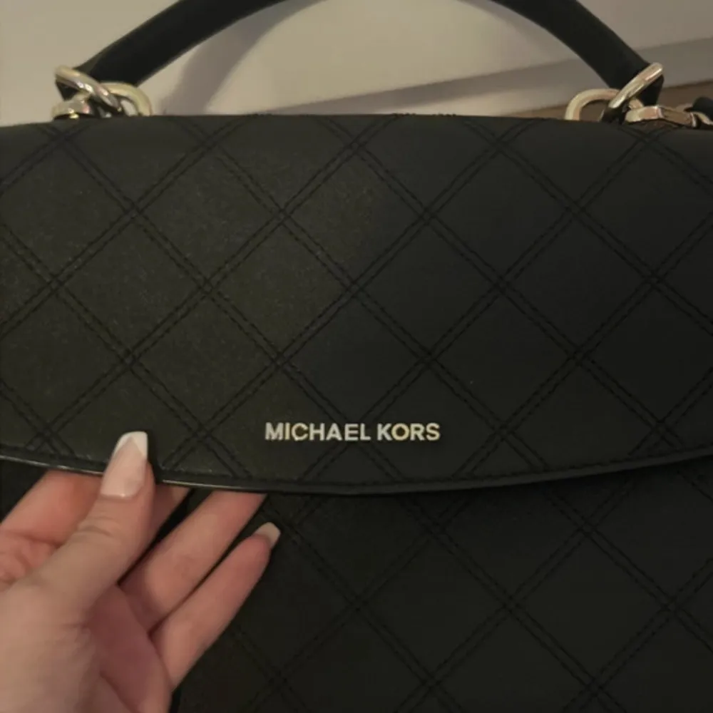 Snygg svart handväska från Michael Kors i quiltat mönster. Väskan har både handtag och en avtagbar axelrem för flexibilitet. Den är i mycket bra skick och har en praktisk dragkedja inuti. Perfekt för både vardag och fest!. Väskor.