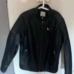 Svart skinnjacka från Jack & Jones - Säljer en snygg svart skinnjacka från Jack & Jones i storlek XL. Jackan har en cool bikerstil med dragkedja framtill och på fickorna. Perfekt för höst och vår. Passar både till vardags och fest! Helt landvind och papperet sitter även kvar på dragkedjorna