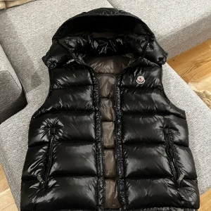 Svart Moncler väst  - Snygg svart dunväst från Moncler i mycket bra skick. Västen har en glansig finish och en praktisk huva. Perfekt för höst och vinter,  priset kan diskuteras vid snabb och smidig affär 