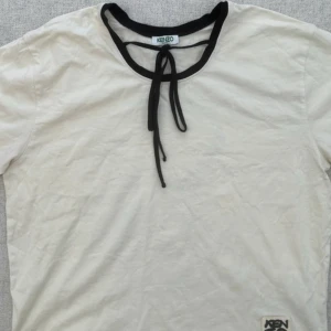 T-shirt - T-shirt från Kenzo med knytband vid kragen. Tryck på ryggen. Storlek XS/34 boxig passform. Nyskick, använt ett par gånger. Finns i Järfälla.