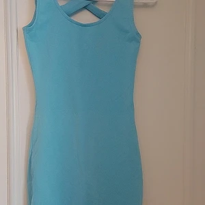 Ljusblå ärmlös klänning från Gina Tricot  - Säljer en superfin ljusblå klänning i ett mjukt och stretchigt material. Den är ärmlös med en snygg omlott-detalj på ryggen som ger en extra touch. Perfekt för sommardagar eller en avslappnad vårlook. Klänningen har en tight passform som framhäver figuren.