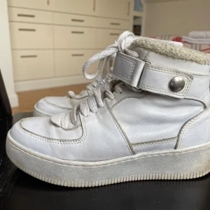 Vita lädersneakers från Hope med teddyfoder - Säljer ett par vita lädersneakers från Hope i bra skick! De har snörning och en justerbar ankelrem med knapp. Insidan är fodrad med teddymaterial och innersulan är av läder. Supersköna och grymt snygga! Sparsmakat använda.