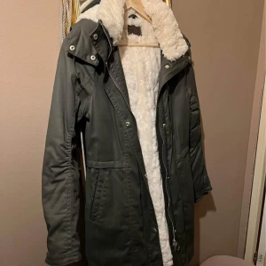 Grön Jofama parkas/kappa/jacka  - Underbar feminin  grön parkas/jacka med coatad (belagd) yta och foder i mjuk fuskpäls.Tyvärr köpt i fel storlek. Nypris ca 3 000kr. Använd 2ggr, så som ny! Perfekt för kyliga dagar. Köparen står för frakten