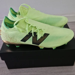 Limegröna fotbollsskor från New Balance - Snygga limegröna fotbollsskor från New Balance med svart logotyp på sidan. Skorna har snörning och en modern design med en lätt och flexibel sula. Perfekta för att dominera på planen med stil. Plus dom e helt nya och andvända på endast en träning.