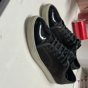 Svarta sneakers från Lanvin - Snygga svarta sneakers från Lanvin med glansig tå och snörning. Skorna har en vit sula och är perfekta för en stilren look. De kommer med originalförpackning.