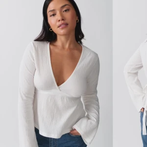 Vit omlottopp med knytband - Snygg vit omlottopp med djup v-ringning och långa ärmar. Toppen har ett knytband i ryggen för en justerbar passform. Perfekt för en stilren look.