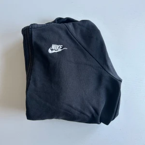 Svart hoodie från Nike - Säljer en svart hoodie från Nike med dragkedja och huva. Tröjan har en liten vit Nike-logga på bröstet. Perfekt för en avslappnad stil. Hör av er vid minsta fundering!