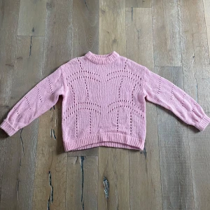 Rosa stickad tröja - Säljer en söt rosa stickad tröja med ett unikt hålmönster. Tröjan har långa ärmar och ribbstickade muddar vid ärmslut och nederkant. Den är från ginatricot i strl. M