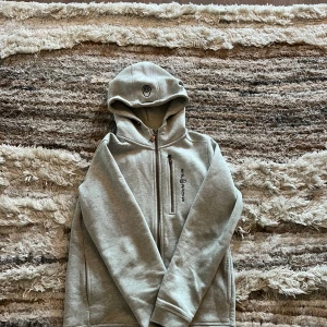 Grå hoodie från Sail Racing - Säljer en stilren grå hoodie från Sail Racing. Den har en dragkedja framtill och en praktisk huva. Perfekt för kyliga dagar och ger en avslappnad look. Passar bra till både jeans och träningsbyxor. Nypris 1000