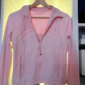 Ljusrosa jacka från Lululemon (define jacket) - Säljer en ljusrosa jacka från Lululemon med dragkedja framtill och två fickor med dragkedjor.  Endast använd ett fåtal gånger, super snygg. Superbra skick. Detta är den kortare modellen. Pris kan diskuteras.