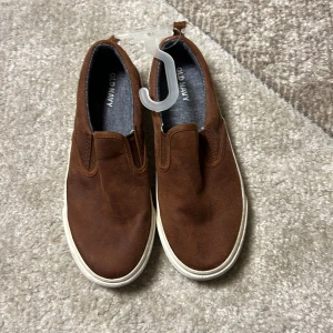 Bruna slip-on skor från Old Navy - Snygga bruna slip-on skor från Old Navy med vit sula. Perfekta för en avslappnad stil. Skorna har en enkel design utan snörning, vilket gör dem lätta att ta på och av.