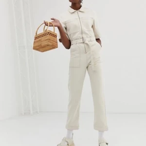 Beige jumpsuit med dragkedja - Snygg beige jumpsuit med korta ärmar och dragkedja framtill. Den har en hög midja och praktiska fickor. Perfekt för en stilren look. Perfekt för dig som vill customiza! Köpt second hand, aldrig använts. Mindre skavanker. 