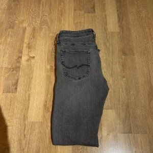 Jack and Jones jeans - Snygga grå jeansbyxor med en klassisk femficksdesign. De har en rak passform och är perfekta för en avslappnad stil. Midjan är normalhög och byxorna har en dragkedja och knapp framtill. Dessa sitter också slim.