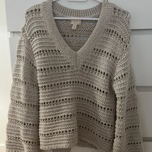 Beige stickad tröja från H&M - Säljer en beige stickad tröja från H&M med v-ringning och ett luftigt mönster. Tröjan har långa ärmar och en avslappnad passform. 