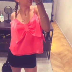 Rosa axelbandslös topp med stor rosett - Säljer en söt rosa axelbandslös topp med en stor rosett framtill. Perfekt för en somrig look eller en festlig kväll. Toppen har en lös passform och är gjord i ett lätt material.