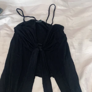 Svart linnetopp med knytning från Gina Tricot - Snygg svart linnetopp från Gina Tricot med smala axelband och knytning framtill. Perfekt för en stilren look. Passar bra till både jeans och kjol.