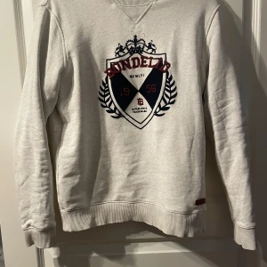Tröja Bondelid - Säljer en stilren beige tröja från Bondelid med ett broderat emblem och mocka på framsidan . Perfekt för en avslappnad stil.