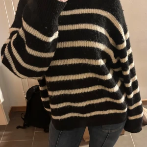 Randig stickad tröja - Mysig och varm stickad tröja med svarta och vita ränder. Tröjan har en avslappnad passform och långa ärmar, perfekt för kyligare dagar. Den är enkel att matcha med jeans eller leggings för en avslappnad look.